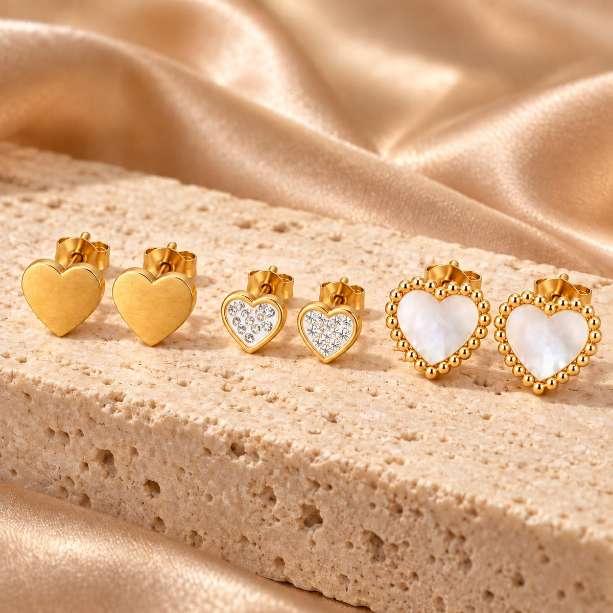 Tres pares de pendientes dorados de corazones sobre piedra beige
